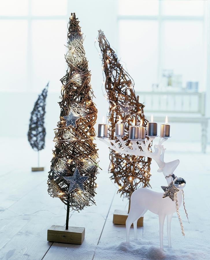 Lit Pillar Candles On White, Stag-shaped Candle Holder In Front Of Two Small, Wicker, Christmas Tree Ornaments Photograph by Matteo Manduzio