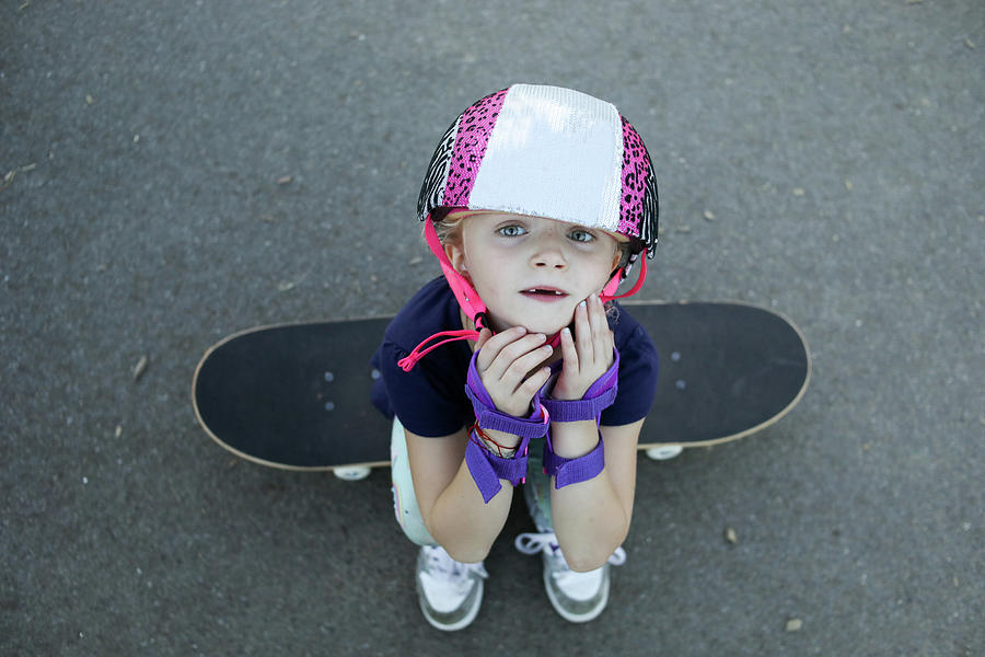 Little Girl Sitting On Skateboarding Looking Up At Camera Photograph by ...