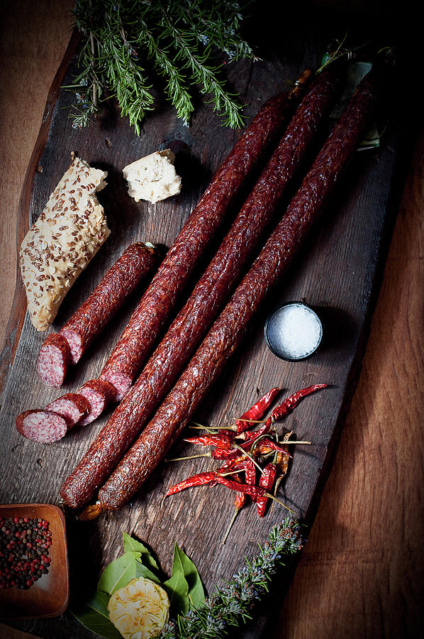 Long Pork Sausages With Flaxseed Rolls And Dried Chilli Peppers On A Wooden Chopping Board Photograph by Tomasz Jakusz