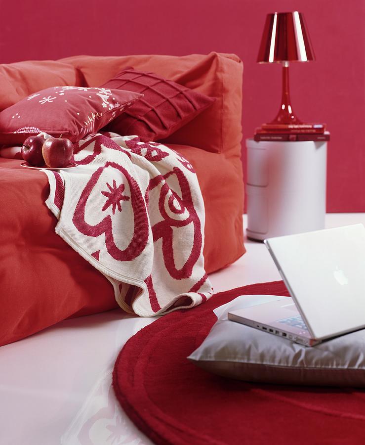 Loose-covered Sofa With Cosy Blankets And Scatter Cushions In Red And White Interior; Laptop On Grey Cushion On Floor Photograph by Matteo Manduzio