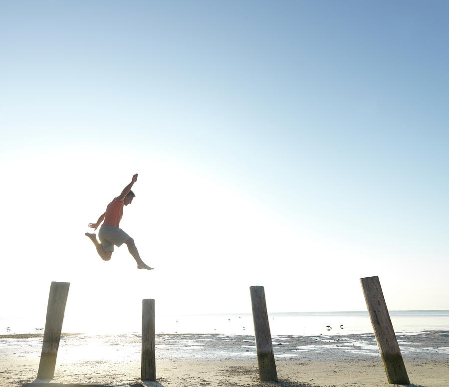 Man Jumps From Post To Post Above Beach Photograph by Ascent/pks Media Inc.