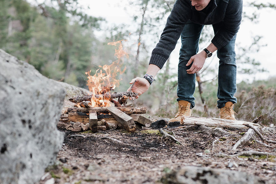 Nature Photograph - Man Putting Sticks On A Campfire Outdoors In Sweden by Cavan Images
