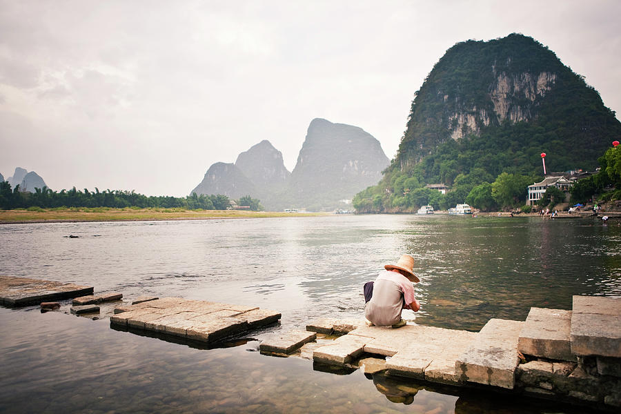 Man Squatting By Li River Photograph by Merten Snijders