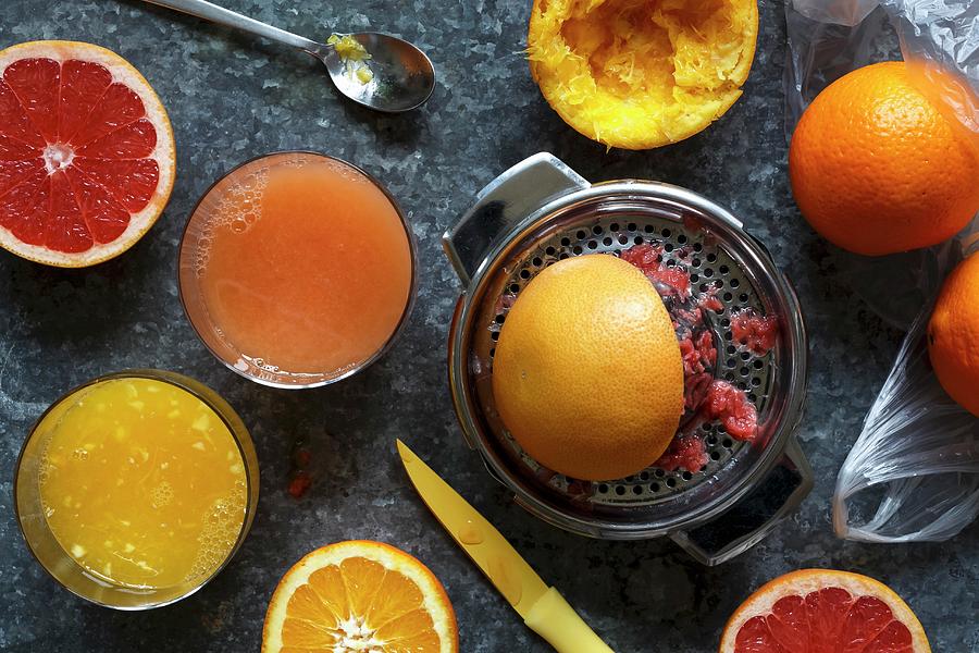 Manual Metal Citrus Fruit Extractor Next To Glasses Of Orange Juice And Red Grapefruit Juice And Whole And Half Cut Oranges And Red Grapefruit Photograph by Etienne Voss
