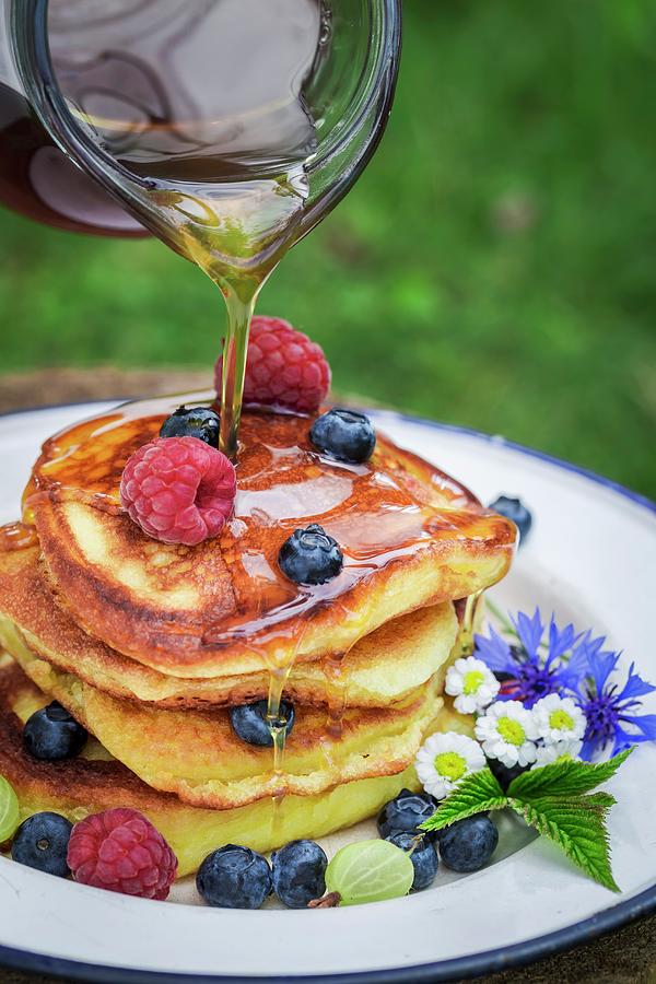 Maple Syrup Being Drizzled On A Pile Of Pancakes With Fresh Berries Photograph by Shaiith