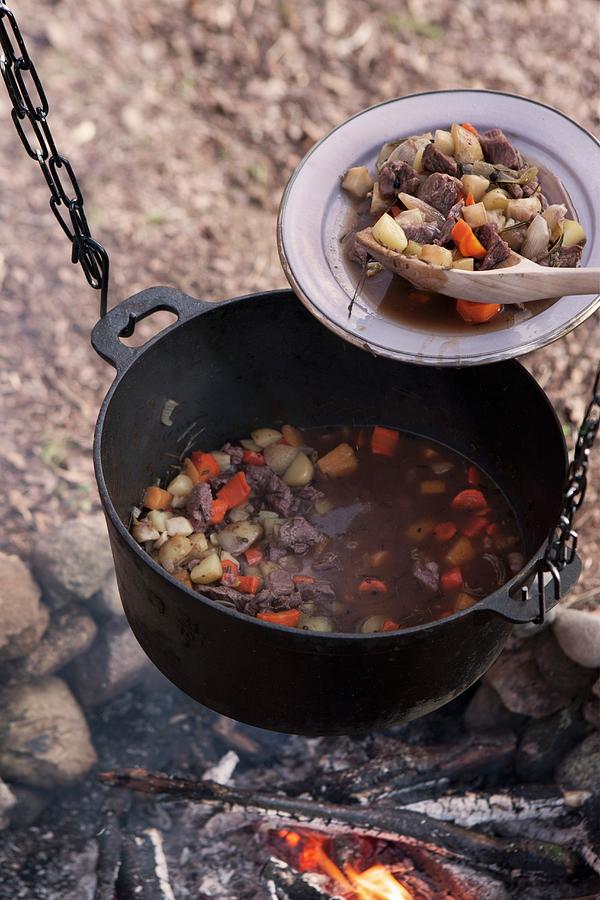 Meat Stew In Bowl And In Iron Cooking Pot Suspended Over Campfire Photograph by Annette Nordstrom