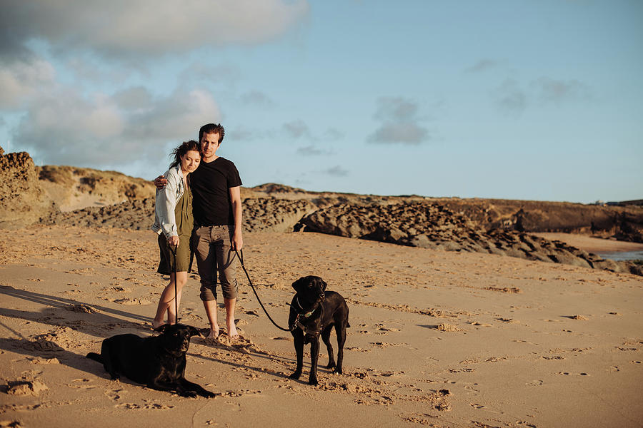 Dog Photograph - Millennial Couple Standing At Beach With Two Black Labradors by Cavan Images