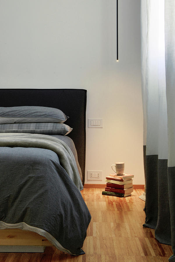 Minimalist Ceiling Light Illuminating Stack Of Books Next To Bed Photograph by Pier Maulini
