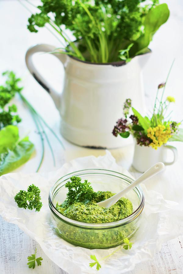 Mixed Herb Pesto In A Glass Bowl, With A Jug Of Herbs In The Background Photograph by Mariola Streim