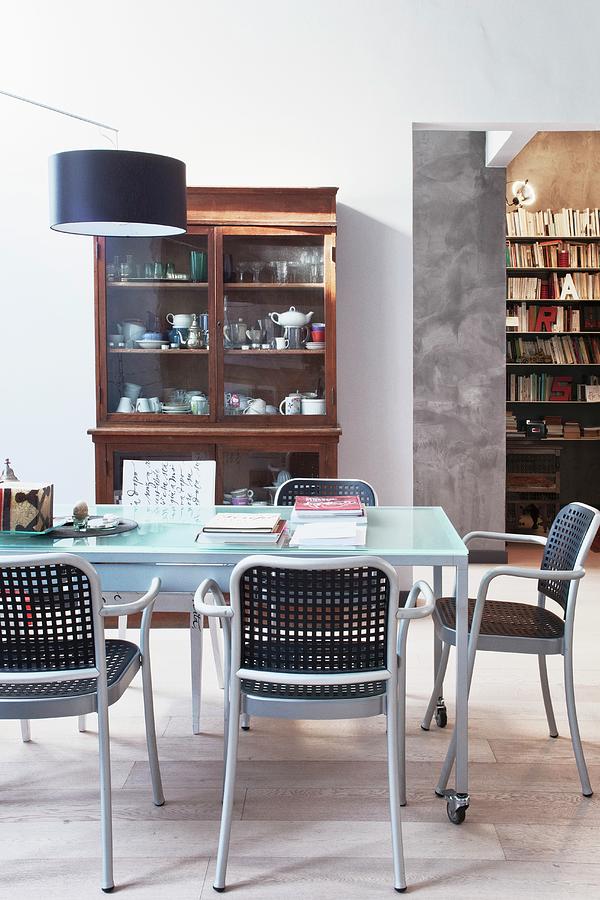 Modern Chairs With Latticed Seats And Backrests, Glass Table On Castors And Designer Lamp In Front Of Antique Display Case And Bookcase In Background Photograph by Fabio Lombrici
