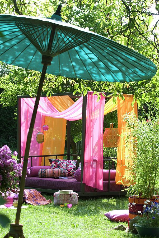 Modern Couch With Canopy Of Pink And Orange Fabrics In Sunny Garden; Oriental Bamboo Parasol In Foreground Photograph by Matteo Manduzio