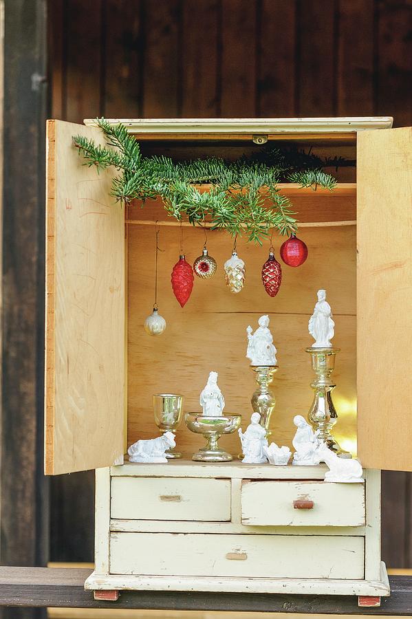 Modern Nativity Scene Arrangement Of White-painted Nativity Set Figurines, Old Christmas Tree Decorations, Mercury Silver Candlesticks And Green Fir Branches In Vintage Dolls-house Cabinet Photograph by Patsy&christian