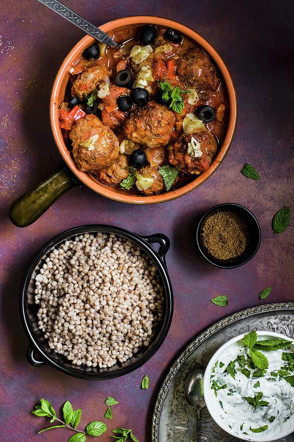 Moroccan Lamb Meatballs In A Spicy Tomato Sauce With Caraway, Garlic And Olives Next To A Bowl Of Giant Couscous Photograph by Magdalena Hendey