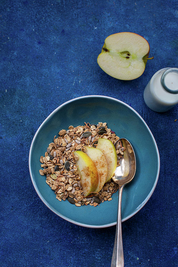Muesli With Apple Wedges On A Blue Plate On A Blue Surface Photograph by Lara Jane Thorpe