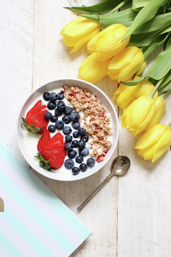 Muesli With Yoghurt, Blueberries And Strawberries Next To A Bunch Of Yellow Tulips Photograph by Sylvia E.k Photography