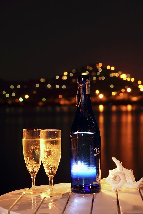 Nighttime Atmosphere With Two Glasses And Bottle Of Sparkling Wine On Table By The Sea Photograph by Angelica Linnhoff