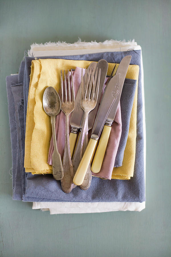 Old Cutlery On Stack Of Pastel Cloths Photograph by Alicja Koll