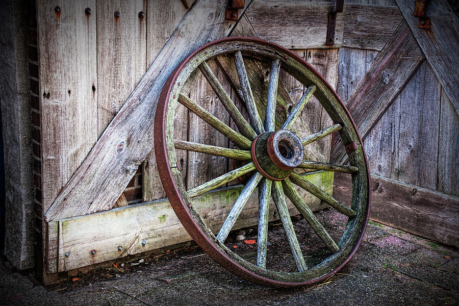 Old Rustic Wooden Wagon Wheel leaning against an old Barn Door Photograph by Randall Nyhof