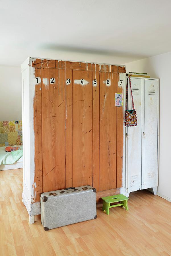 Old Wardrobe And White Metal Lockers Used As Partition; Numbers Painted On Back Of Wooden Wardrobe With Vintage Suitcase And Green Footstool On Floor Photograph by Revier 51
