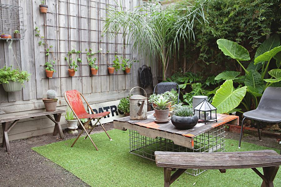 Old Wooden Bench And Hand-made Table In Courtyard Decorated With Many Potted Plants And Artificial Grass Rug Photograph by Natalie Jeffcott