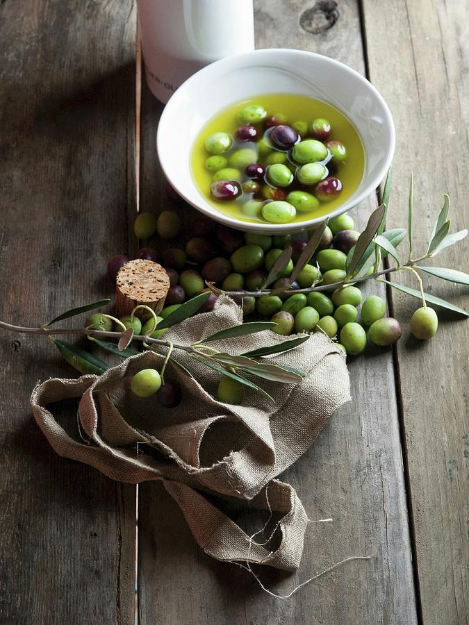 Olives And Olive Oil And A Sprig Of Green Olives On A Rustic Wooden Table Photograph by Riccardobruni