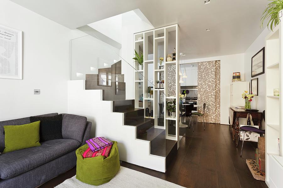 Open-plan Interior With Tall Shelves As Partition And View Of Dark Brown Staircase With Glass Balustrade; Grey Couch And Green Beanbag In Foreground Photograph by Simon Maxwell Photography