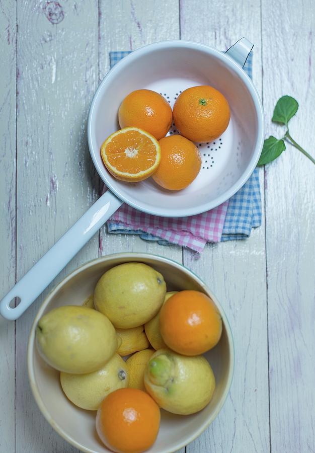 Oranges In An Enamel Colander, Oranges And Lemons In A Porcelain Bowl And Fresh Mint Photograph by Angelika Grossmann