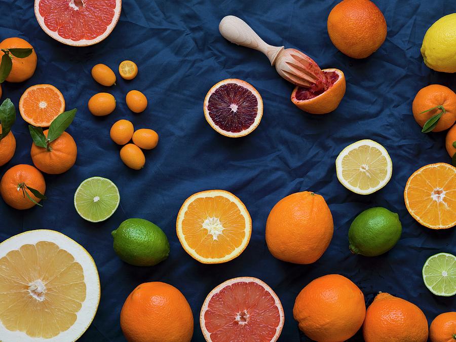 Overhead Of Cut And Whole Grapefruits, Oranges, Lemons, Limes And Kumquats On A Dark Blue Material With A Blood Orange Juiced With A Wood Reamer Photograph by Don Crossland