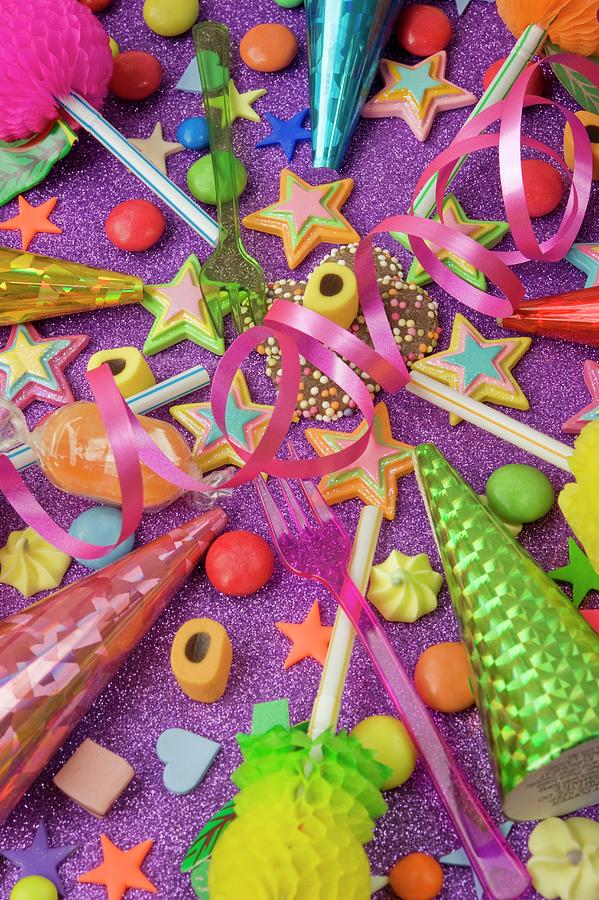 Overview Still Life Of Various Party Decorations, Party Poppers Sweets And Straws For The Party Table On A Purple Glittery Table Photograph by Burgess, Linda