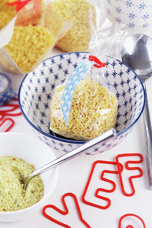 Packets Of Alphabet Noodles In Small Bowls And Red, Alphabet-shaped Elastic Bands Photograph by Franziska Taube