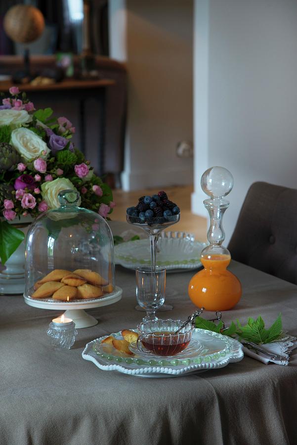Pastries Under Glass Cover And Glass Carafe Of Juice With Spherical Stopper On Set Table Photograph by Christophe Madamour