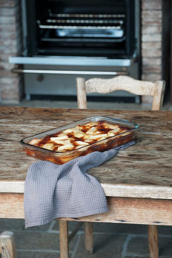 Pear Clafoutis In The Baking Dish On A Wooden Table In Front Of The Oven Photograph by Christophe Madamour
