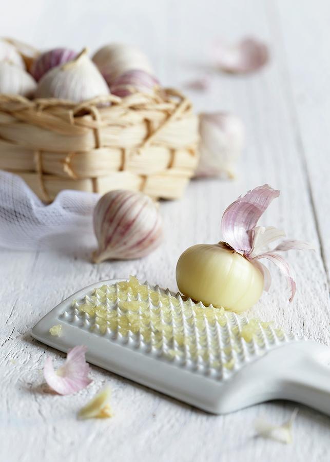 Peeled Single Clove Garlic Grated On A White Ceramic Grater With A Straw Basket Full Of Unpeeled Single Clove Garlics Photograph by Etienne Voss