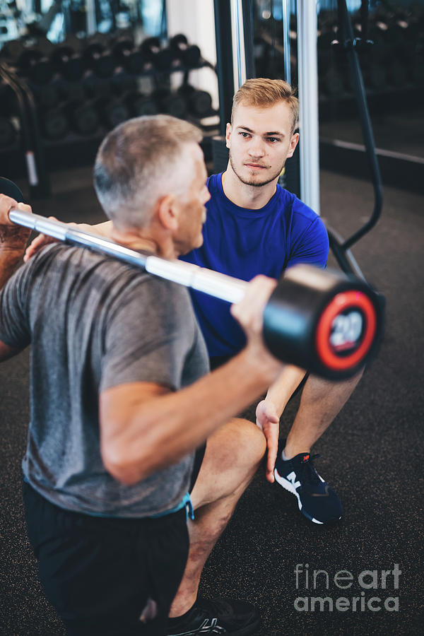 Personal trainer and senior man exercising at the gym. Photograph by Michal Bednarek