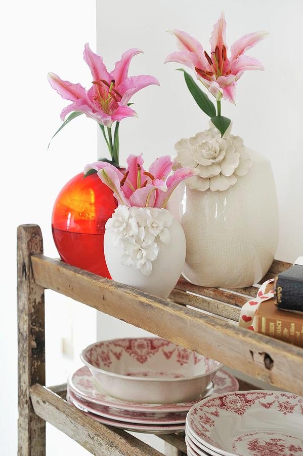 Pink Lilies In White China Vases And Red Glass Vase Next To Traditional Dinner Service On Vintage Wooden Shelving Photograph by Great Stock!