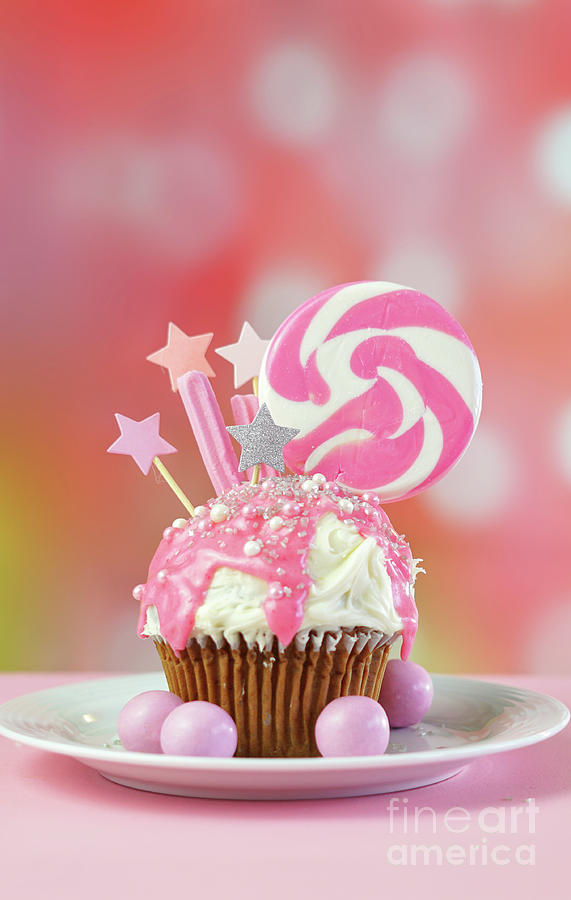 Pink novelty cupcake decorated with candy and large lollipop. Photograph by Milleflore Images