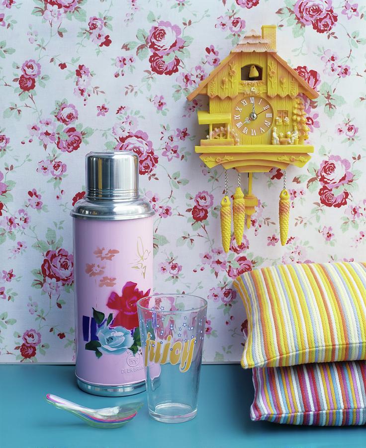 Pink Thermos Flask With Floral Motif Next To Brightly Striped Cushions Below Yellow Cuckoo Clock On Rose-patterned Wallpaper Photograph by Matteo Manduzio