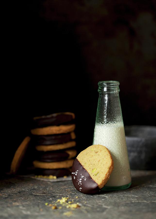 Pistachio Biscuits With Dark Chocolate Glaze And Sea Salt Served With A Bottle Of Milk Photograph by Jane Saunders