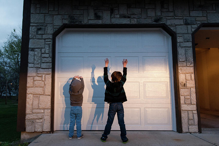 Sunset Photograph - Playful Brothers With Arms Raised Standing In Front Of Door During Sunset by Cavan Images