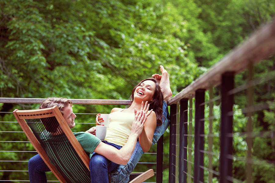 Playful Couple Laughing While Sitting On Chair By Railing Photograph by Cavan Images