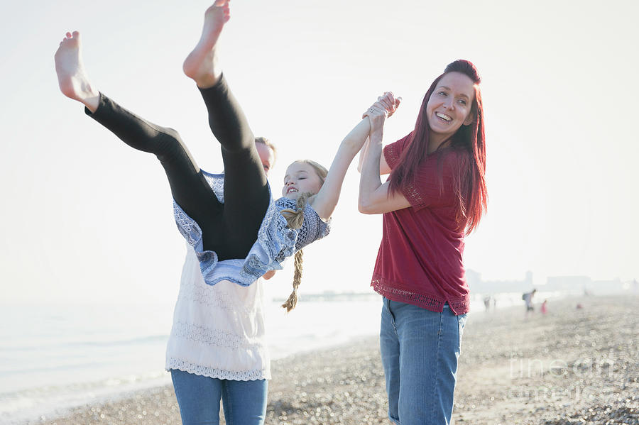 Playful Lesbian Couple Swinging Daughter On Beach Photograph By Caia