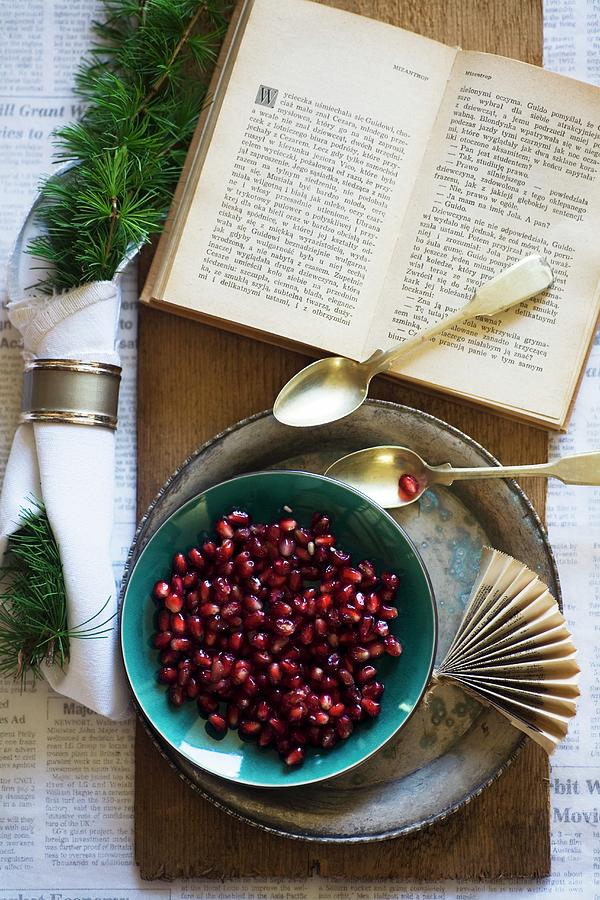 Pomegranate Seeds In A Bowl With A Silver Spoon And An Open Book Photograph by Alicja Koll