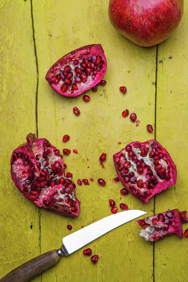 Pomegranates, Whole And Chopped, On A Rustic Yellow Wooden Surface Photograph by Artfeeder