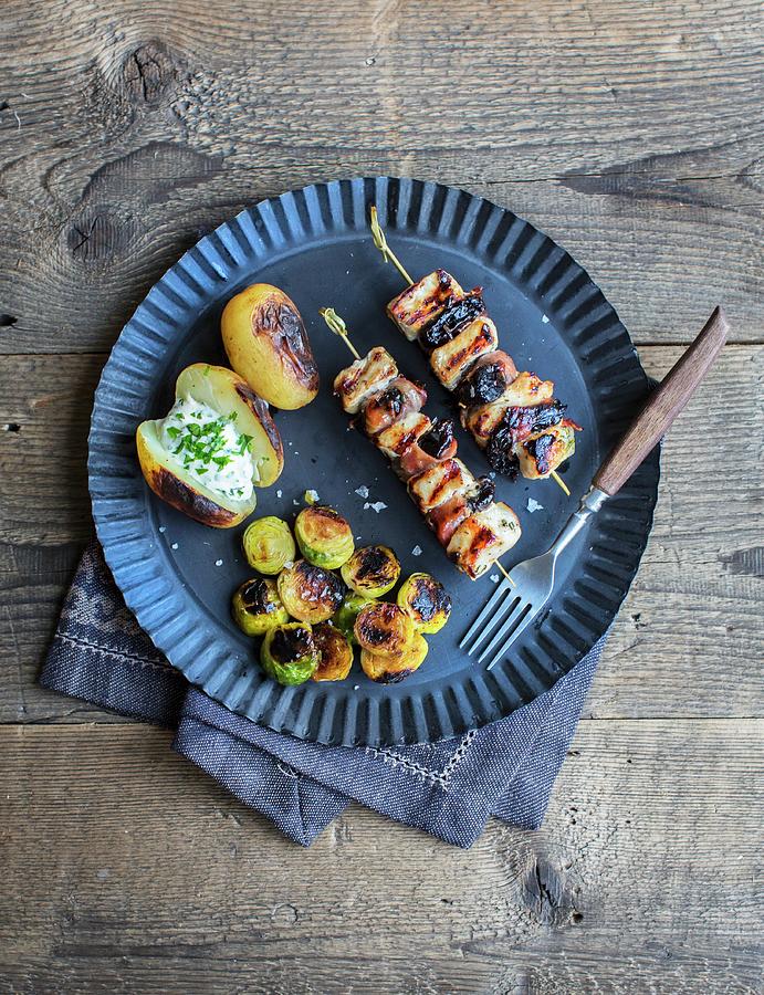 Pork And Bacon Skewers With Dried Plums, Brussels Sprouts And A Baked Potato With Sour Cream Photograph by Anne Faber