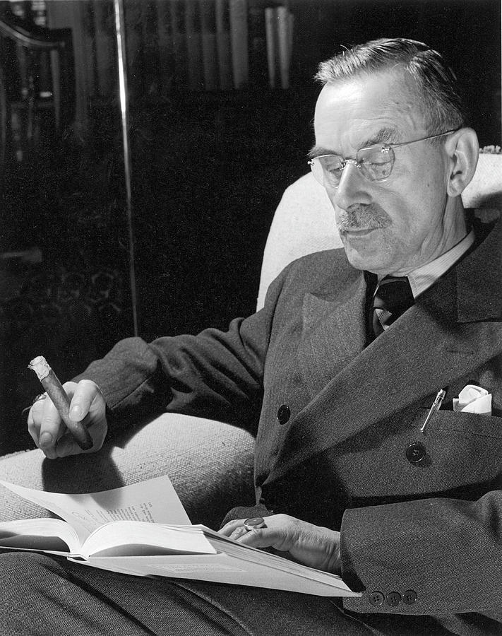 Portrait of German-born novelist Thomas Mann sitting in armchair at home, smoking cigar and reading a book. Photograph by Carl Mydans