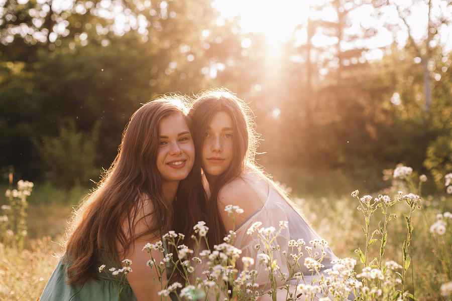 Portrait Of Happy Lesbian Couple Sitting Amidst Flowers In Summer