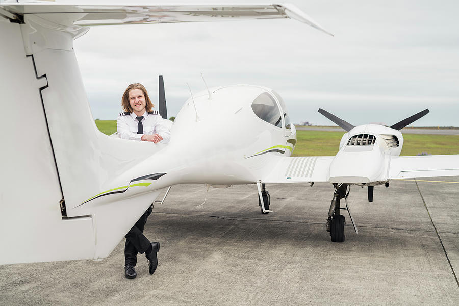 Portrait Of Smiling Male Pilot Standing By Airplane On Airport Runway 