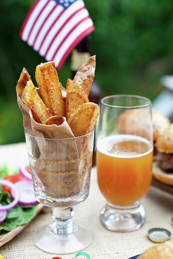 Potato Wedges On A Table Outside, In The Background Buffalo Burgers And A Us Flag Photograph by Strokin, Yelena