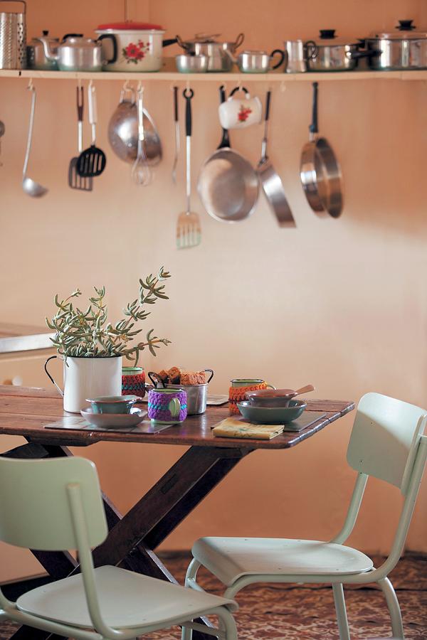 Pots, Pans And Kitchen Utensils On Wall-mounted Shelf Above Dining Table In Kitchen Photograph by Great Stock!
