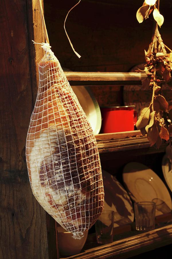 Prosciutto Hanging In A Kitchen Cupboard Photograph by Jean-marc Blache